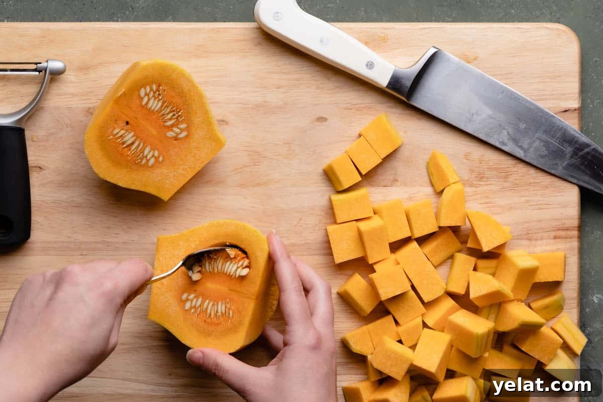 Maple-Glazed Roasted Squash and Apples for Fall Side Dish 6 hand holding small metal spoon scooping seeds out from butternut squash with cubes of squash and knife on the side