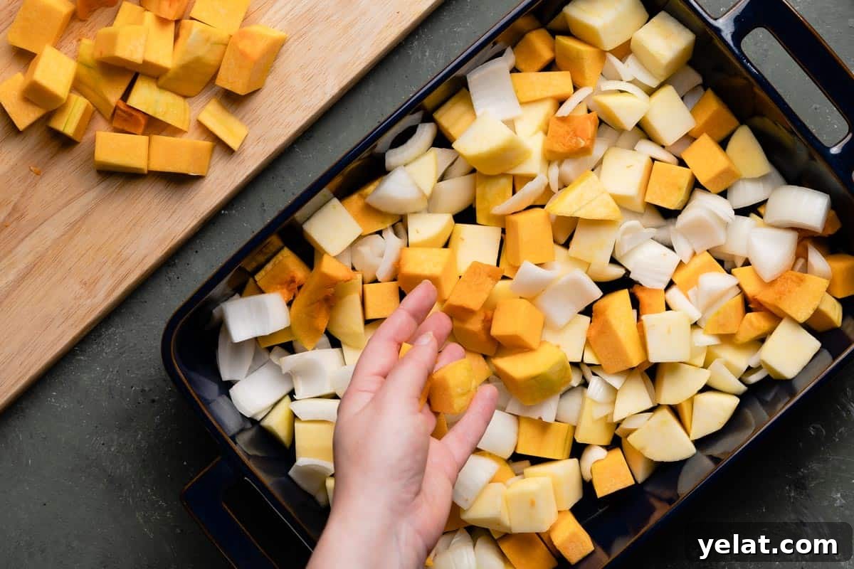 Maple-Glazed Roasted Squash and Apples for Fall Side Dish 7 hand adding a few chunks of butternut squash to pan with chunks of apples onions and butternut squash