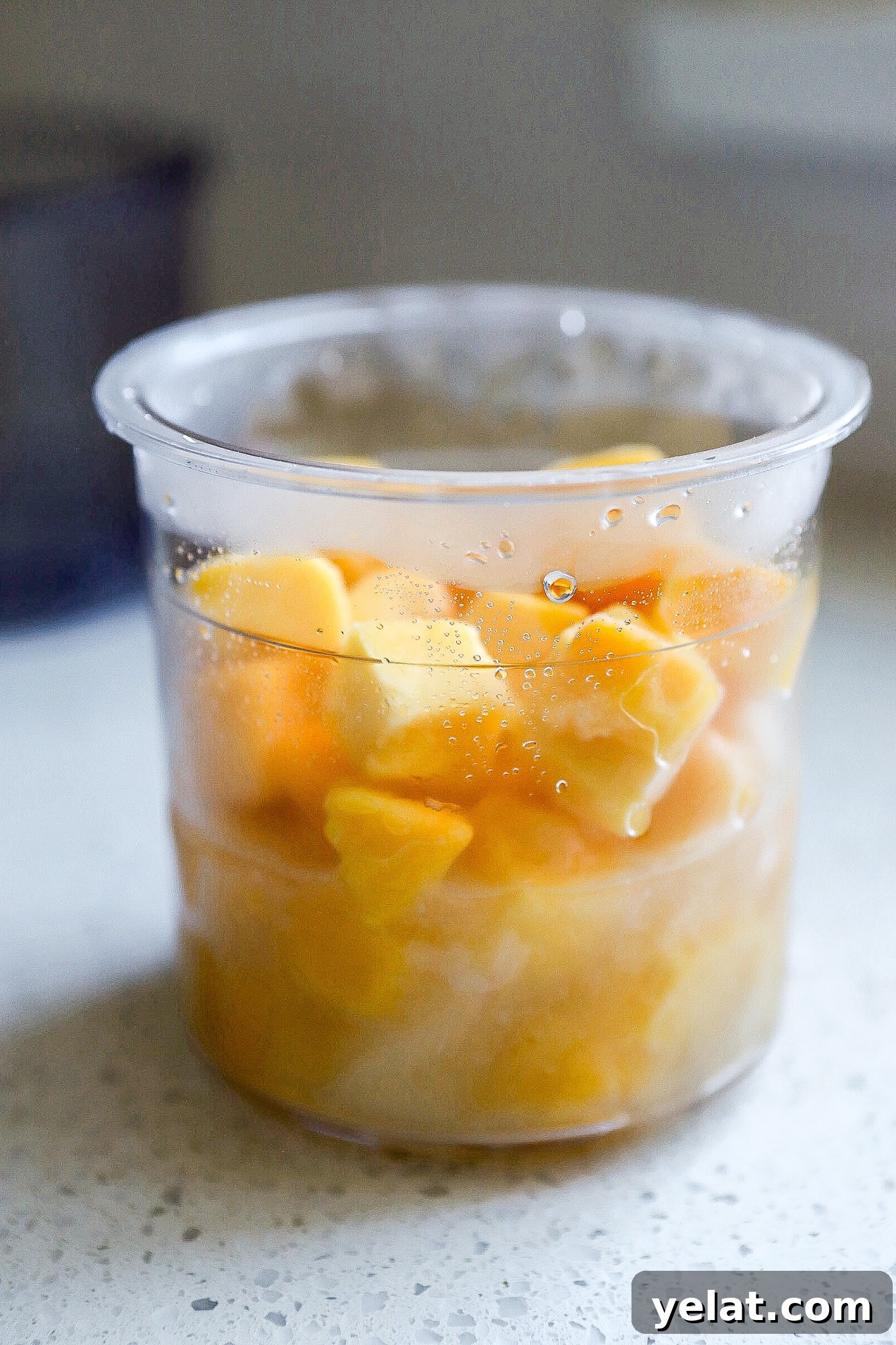 Ninja Creami Mango Sorbet: 3-Ingredient Dairy-Free Recipe 5 Side angle of frozen pineapple chunks in the ninja creami pint container on white kitchen counter.