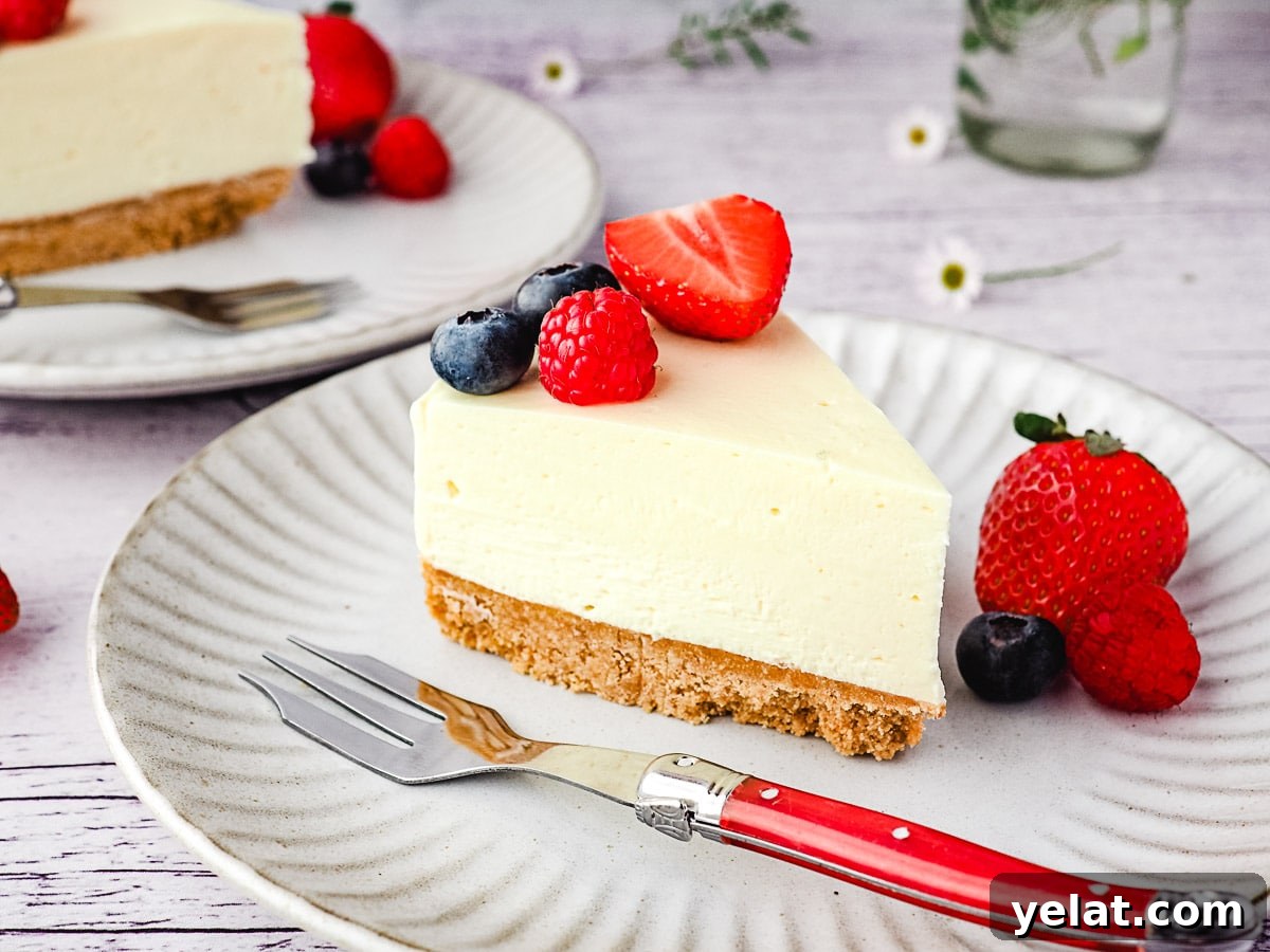 Philadelphia No-Bake Cheesecake Recipe — Creamy, Refrigerator Cheesecake 11 Slice of cheesecake on a plate with fresh berries, with another slice of cheesecake and small vase of flowers in the background.