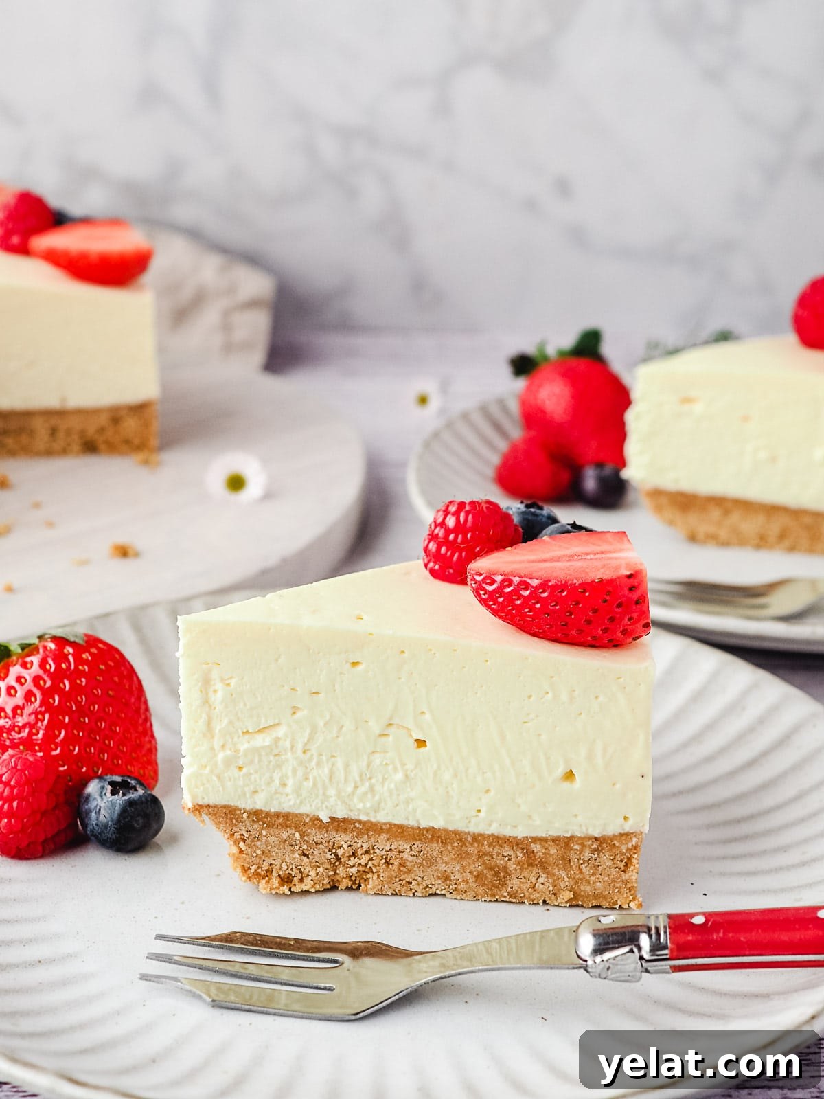 Philadelphia No-Bake Cheesecake Recipe — Creamy, Refrigerator Cheesecake 13 Slice of cheesecake on a plate with fresh berries and rest of cake and another slice of cheesecake in the background.