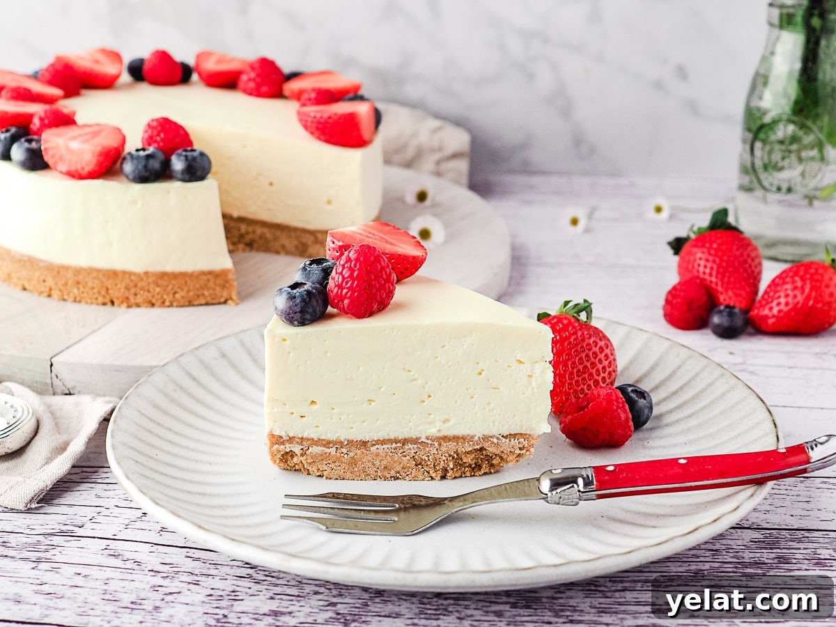 Philadelphia No-Bake Cheesecake Recipe — Creamy, Refrigerator Cheesecake 3 Slice of cheesecake on a plate with fresh berries and rest of cake and a small vase of flowers in the background.