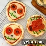 Four baked Halloween personal pizzas decorated as skulls and spiders.
