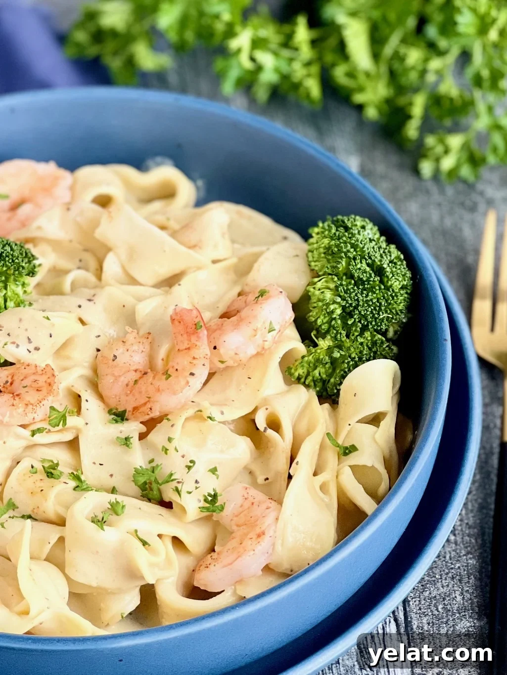 Garlic Shrimp and Broccoli Pasta Recipe for Quick Weeknight Dinners 5 Blue bowl with creamy pasta, sautéed shrimp, and steamed broccoli, garnished with parsley.