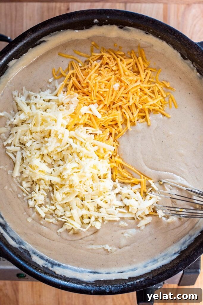 Skillet Buffalo Chicken Macaroni and Cheese Recipe 13 Adding shredded cheddar cheeses to a roux in a cast iron skillet.