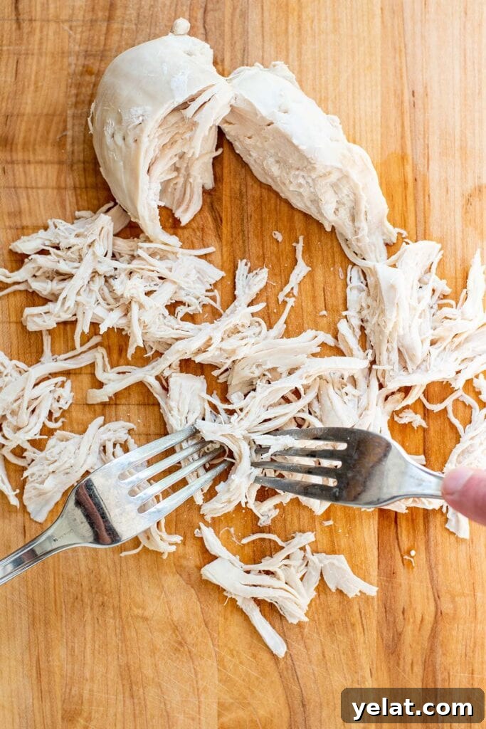 Skillet Buffalo Chicken Macaroni and Cheese Recipe 5 Two forks shredding boiled chicken on a wooden cutting board.