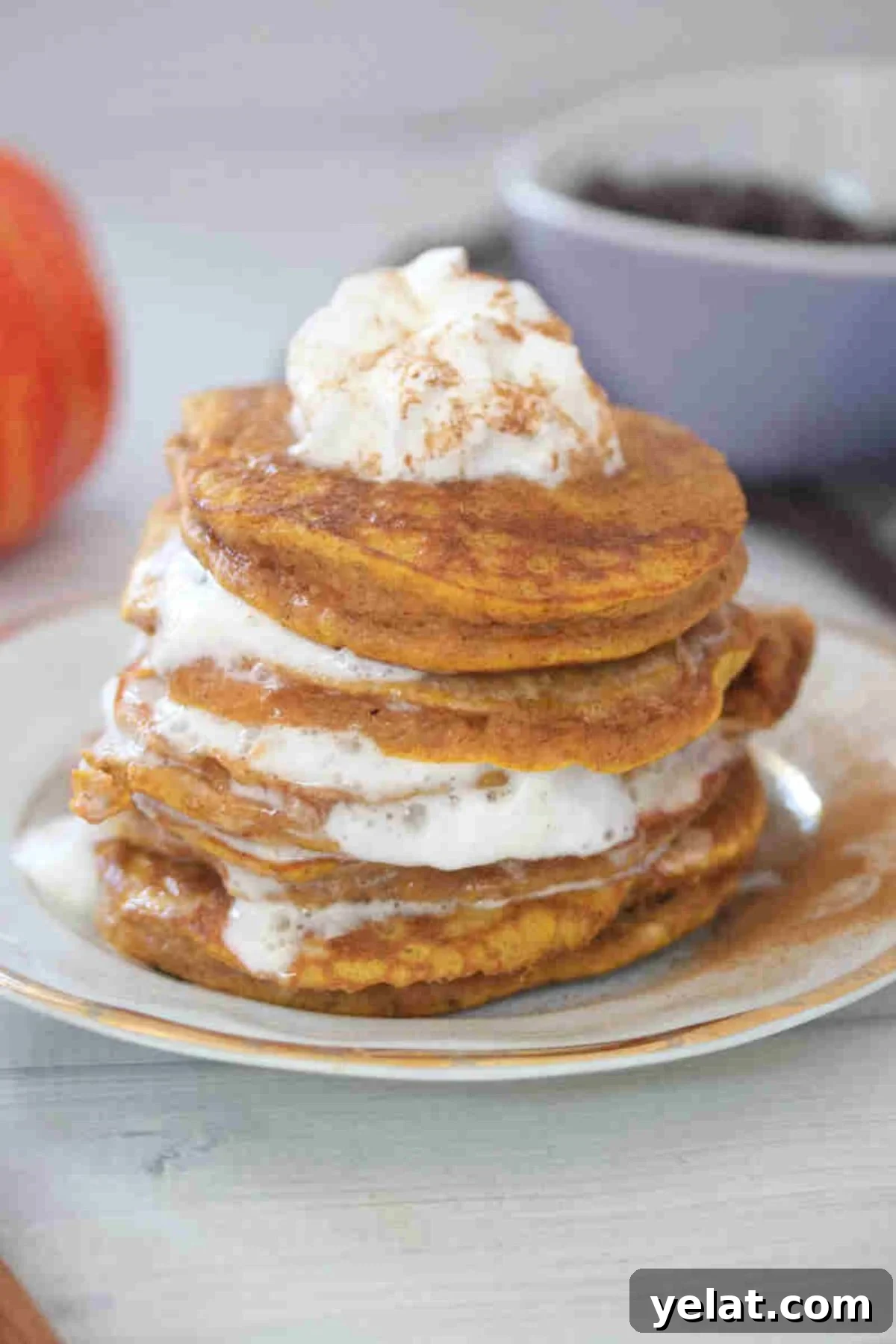 Stacked pumpkin pancakes with layers of whipped cream on a white plate.