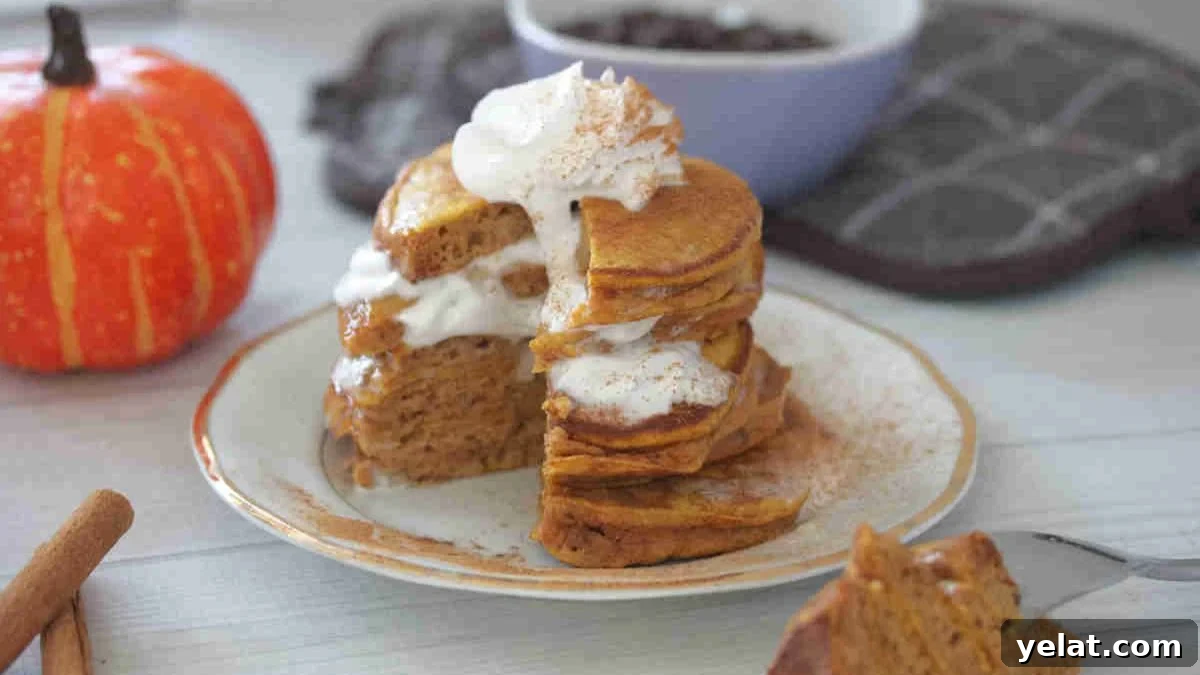Stacked pumpkin pancakes with layers of whipped cream on a white plate with a slice out of the pancakes.