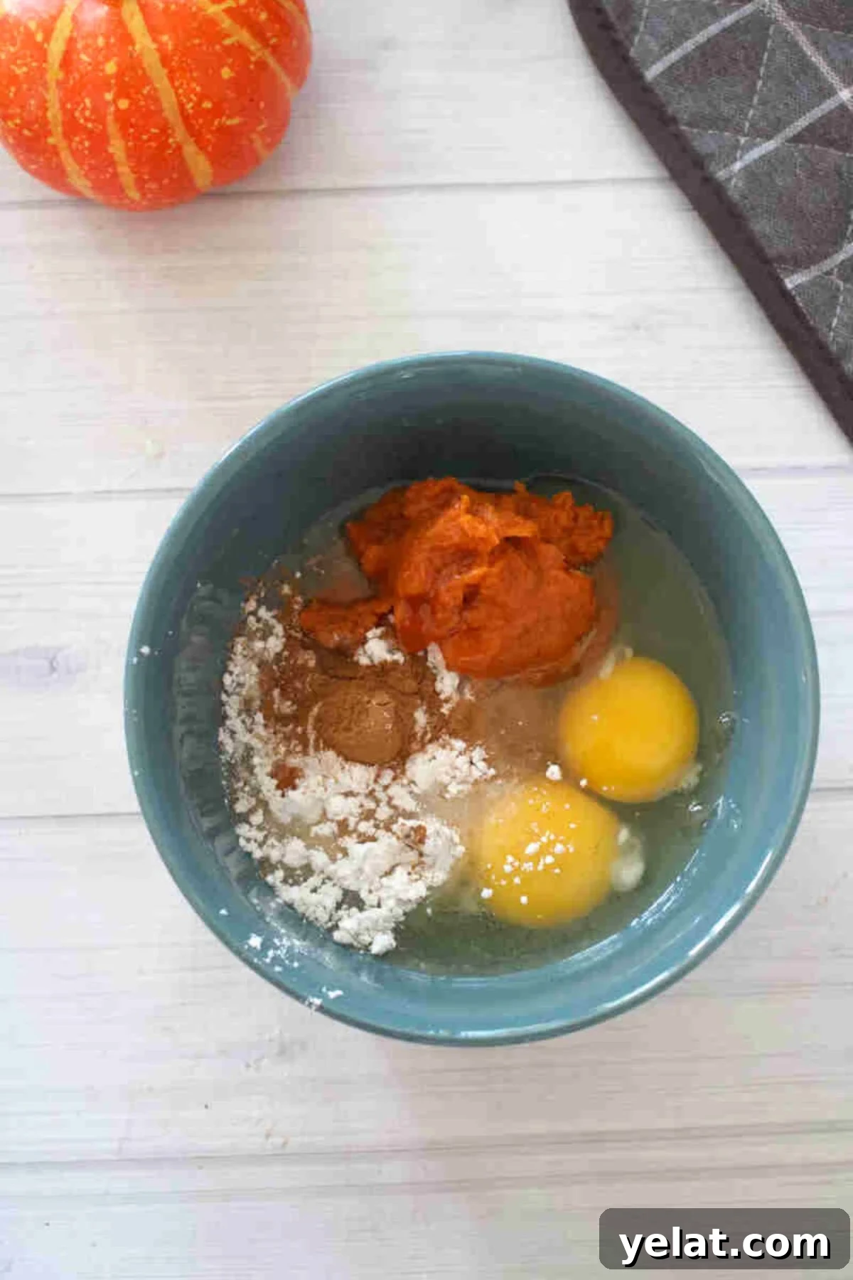 Blue bowl with pumpkin, eggs, and flour in it.