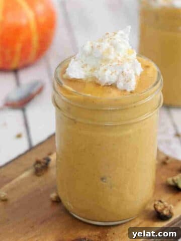 Pumpkin smoothie topped with coconut whipped cream in a mason jar on a wooden cutting board.