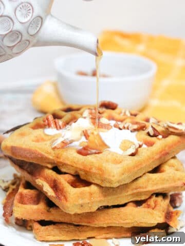 Maple syrup being poured onto stacked pumpkin waffles with coconut cream and pecans