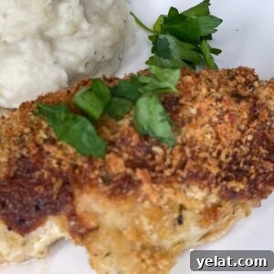A breaded and baked chicken breast topped with chopped parsley, served with a side of mashed potatoes and a sprig of fresh parsley on a white plate.