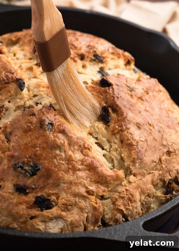 Classic Irish-American Soda Bread Recipe for Homemade Loaves 7 brushing melted butter onto baked soda bread in a cast iron skillet