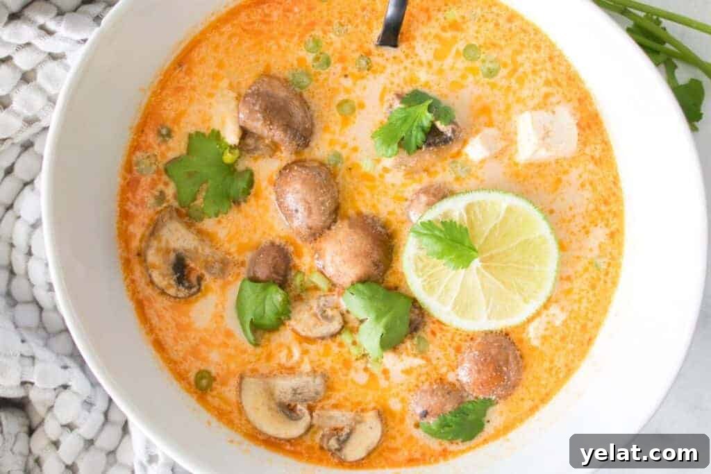 A bowl of Tom Kha Soup with green herbs, and a slice of lime.