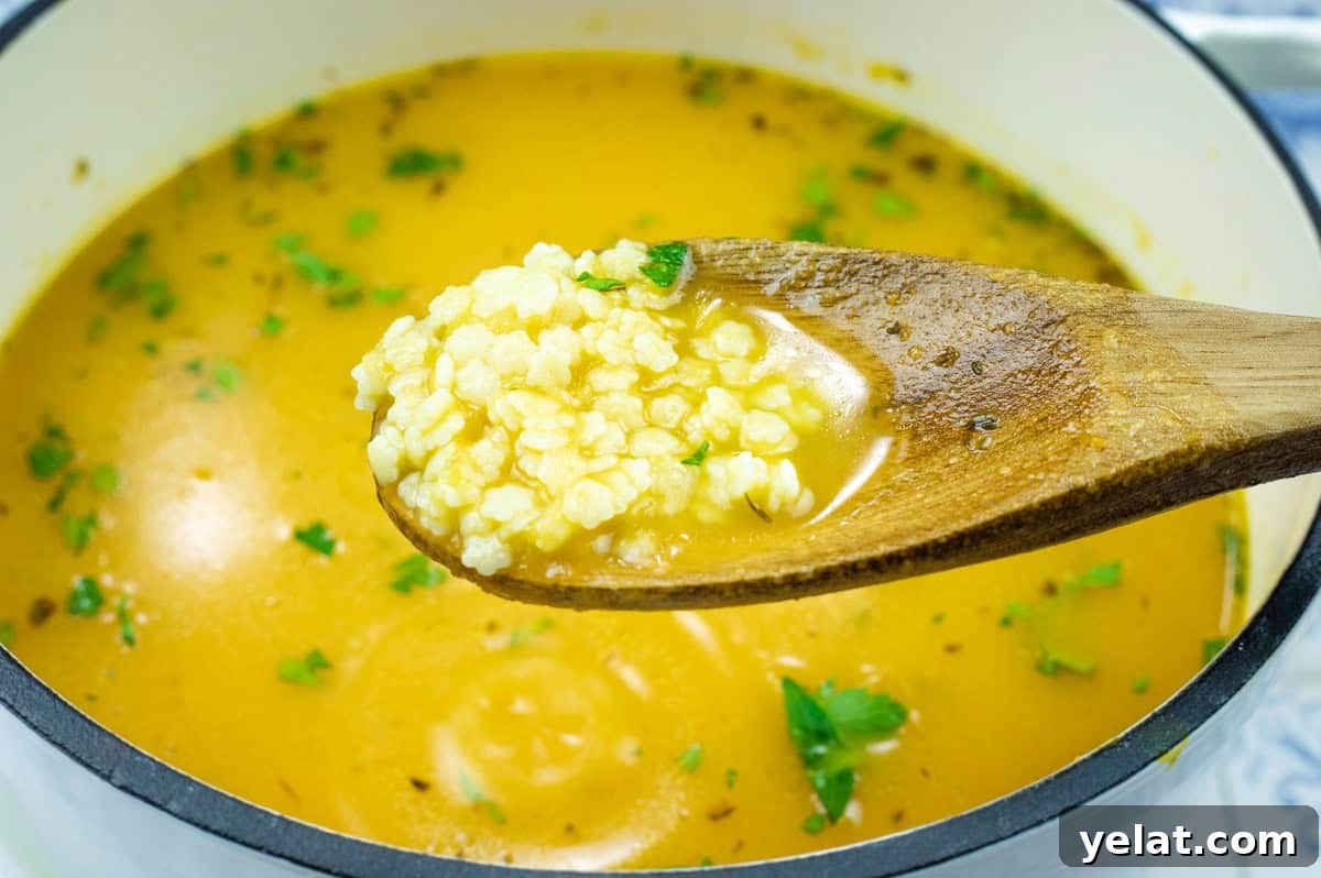 A wooden spoon holds a portion of Pastina Soup hovering above a pot.