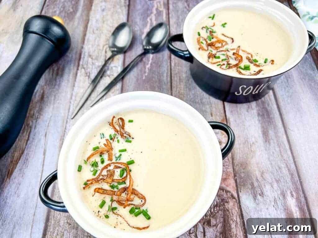 Two bowls of cream of onion soup topped with crispy onions and chives on a wooden table.
