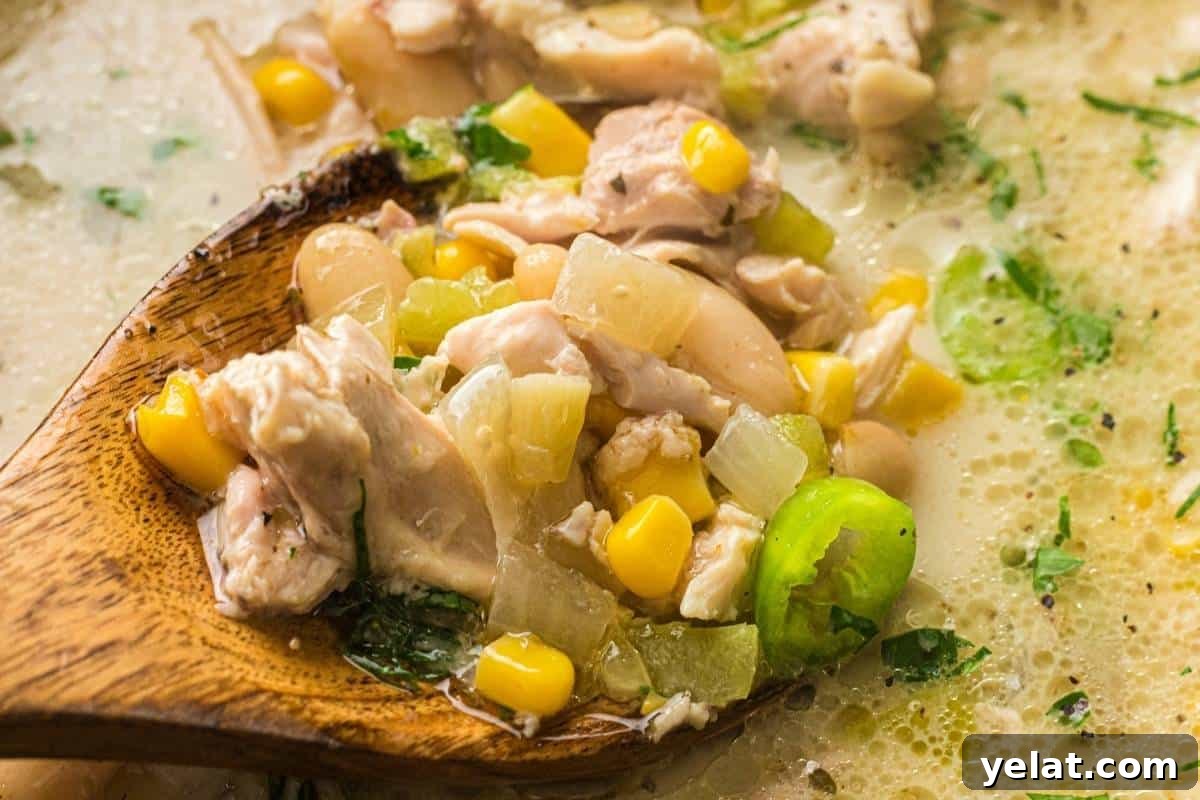 A wooden spoon holding a portion of white chicken chili with corn, beans, onions, and herbs.