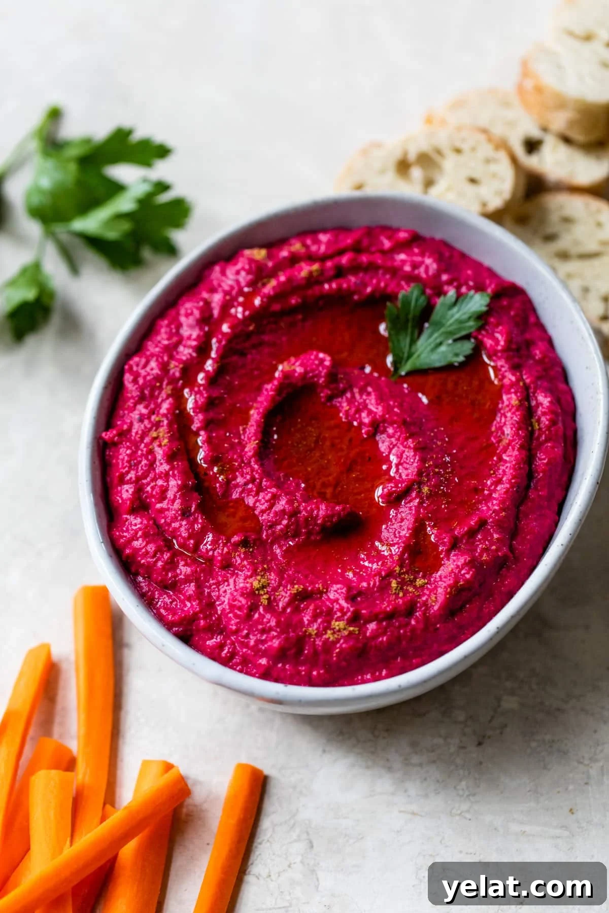 beet hummus in a bowl surrounded by slices of bread and carrots