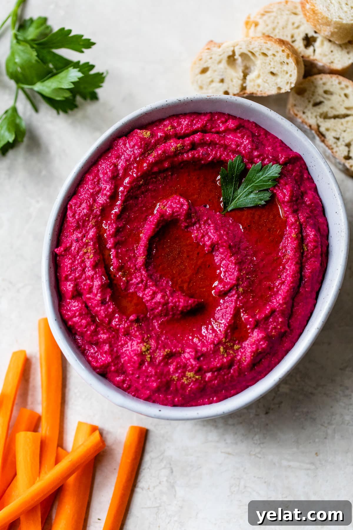 beet hummus in a bowl surrounded by slices of bread and carrots
