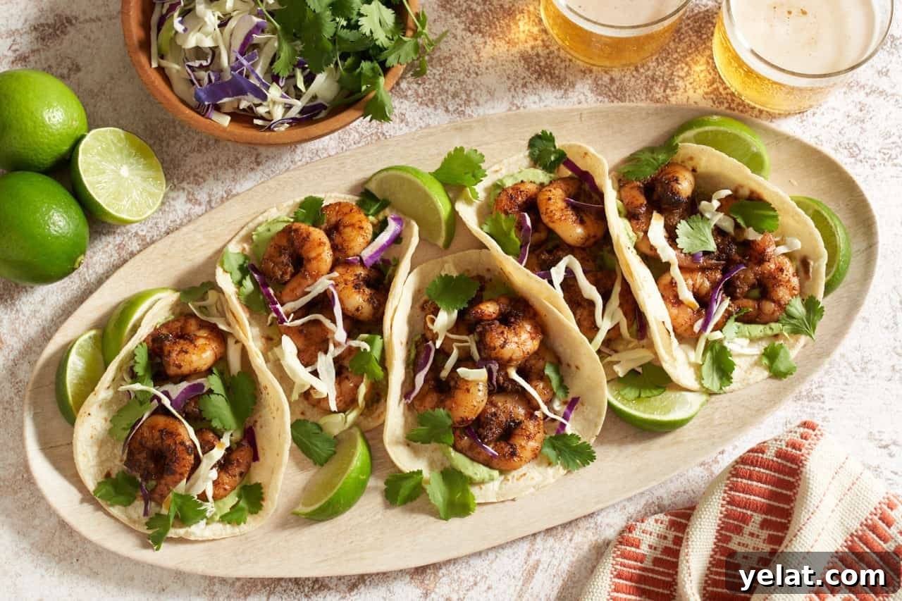 A plate of baja shrimp tacos with lime wedges, surrounded by a glass of beer, a bowl of cabbage and cilantro, and an orange and white towel.