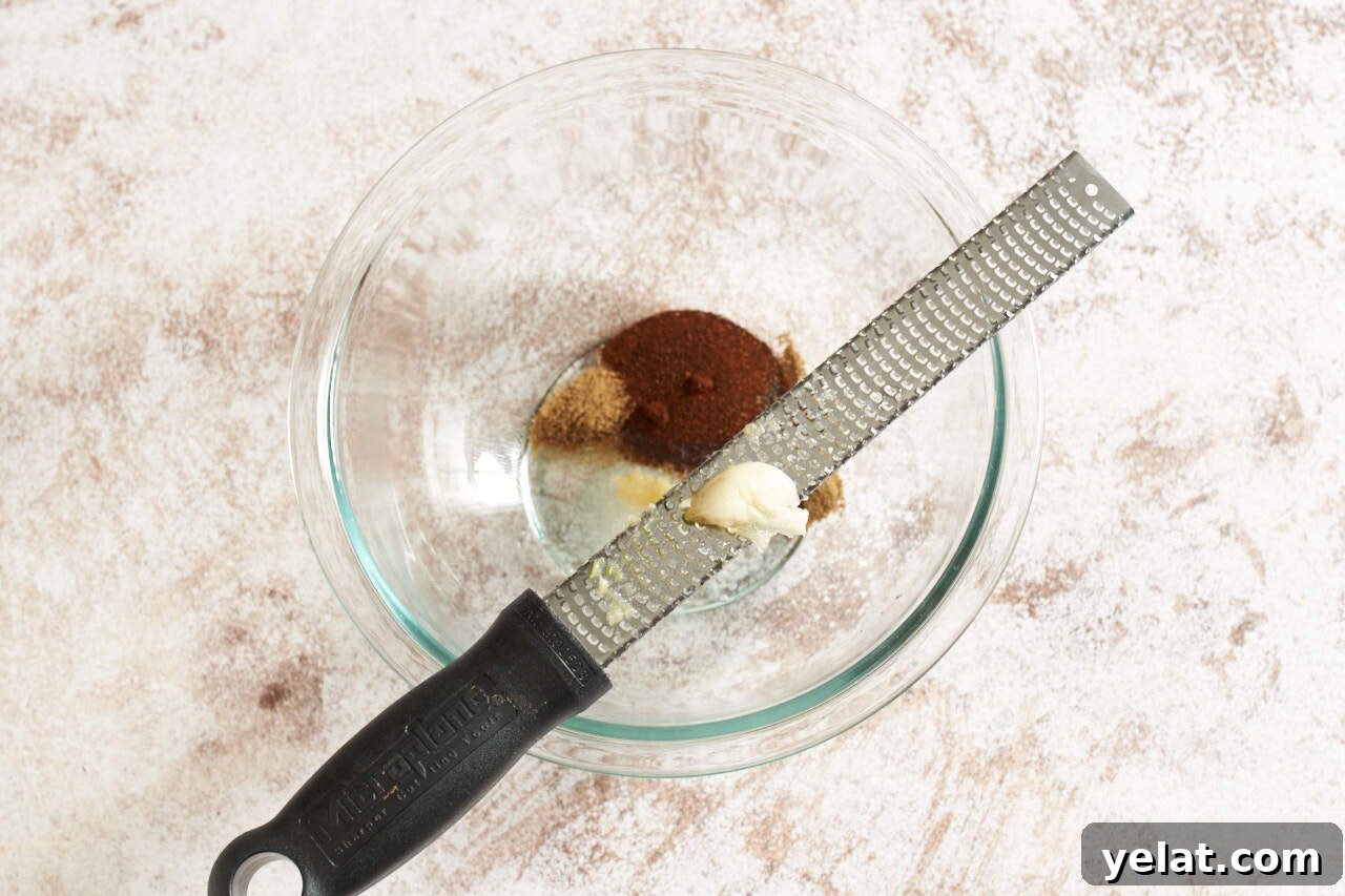 A microplane grater with a garlic clove over a bowl of taco seasoning.