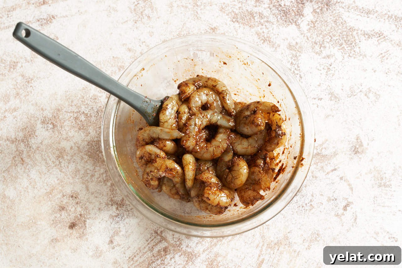 Shrimp in a marinade of taco seasoning in a glass bowl.