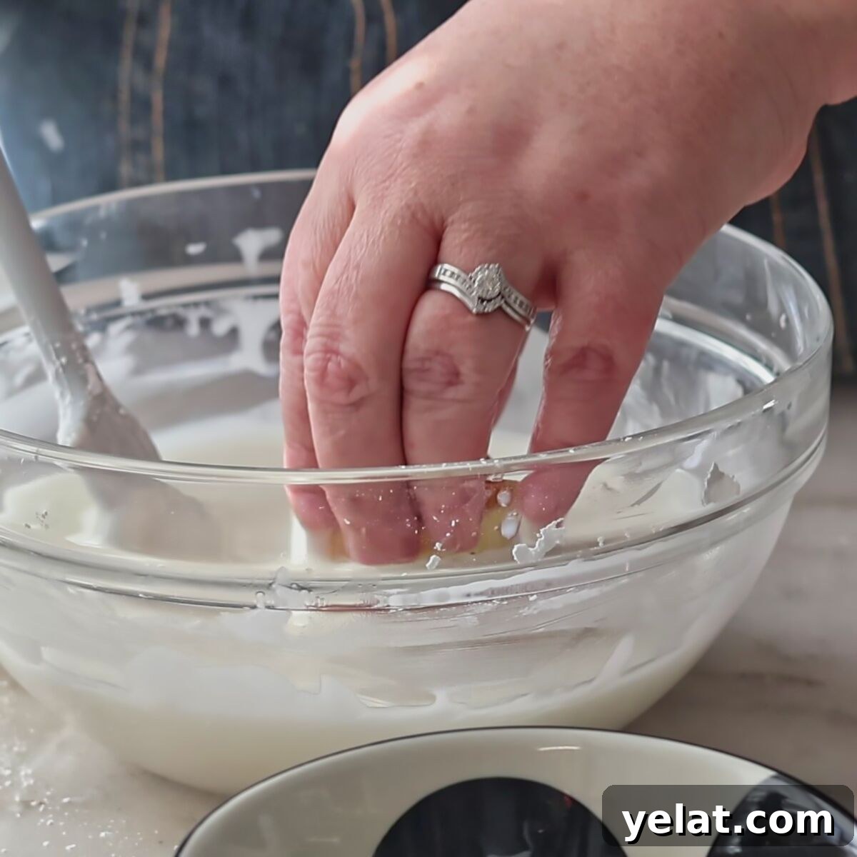 Irresistible Gluten-Free Ricotta Cookie Recipe 11 dunking cookie into white icing in glass bowl.