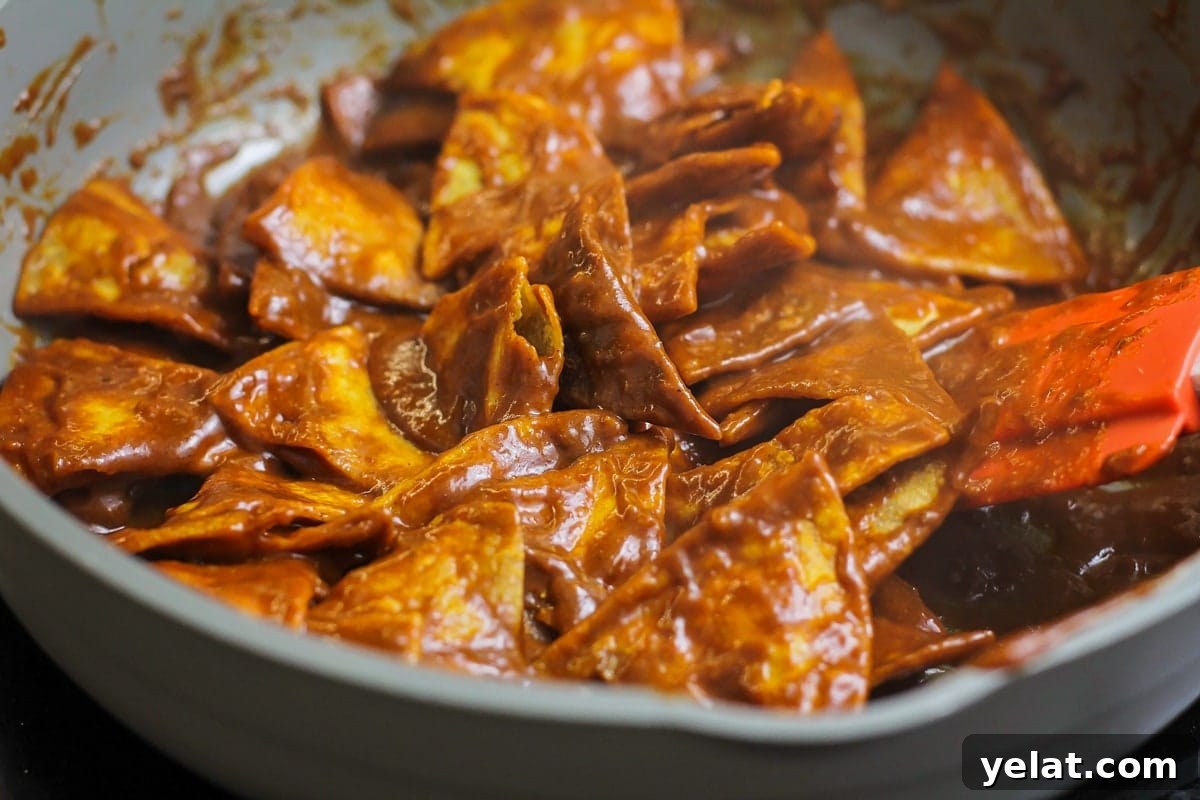 Add a little spice to your breakfast with this authentic chilaquiles recipe - a Mexican classic that's on the table in only 20 minutes! Covering tortilla chips with red enchilada sauce in a pan.