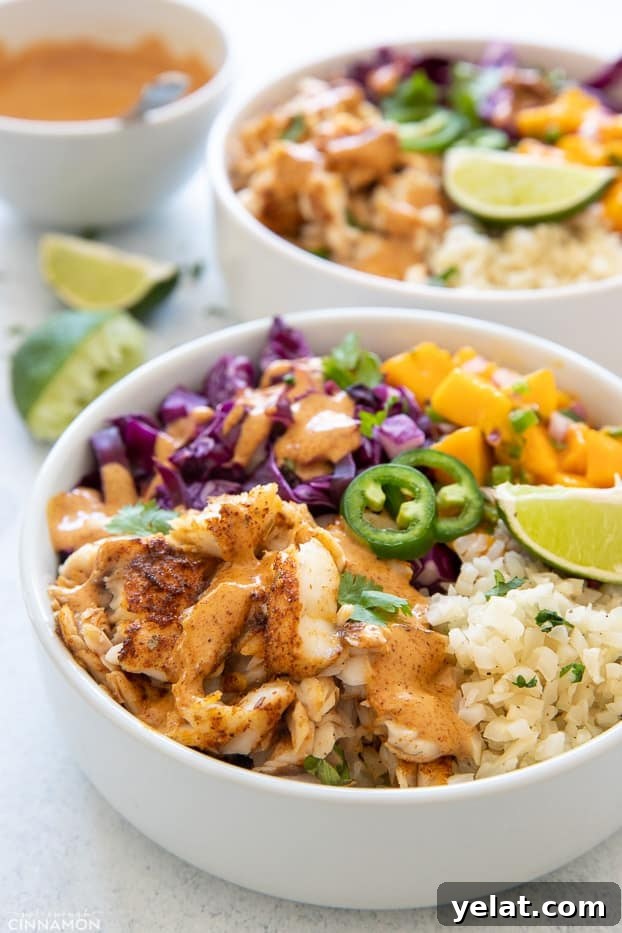 taco bowls side view of a healthy fish taco bowl with cilantro lime cauliflower rice and baked fish fillet drizzled with chipotle mayo