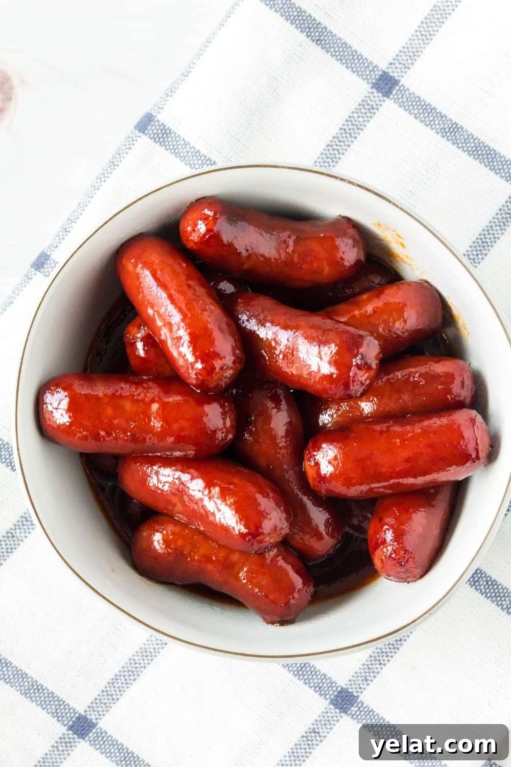 Instant Pot little smokies in bbq grape jelly sauce, served in a white bowl atop a blue and white checked napkin