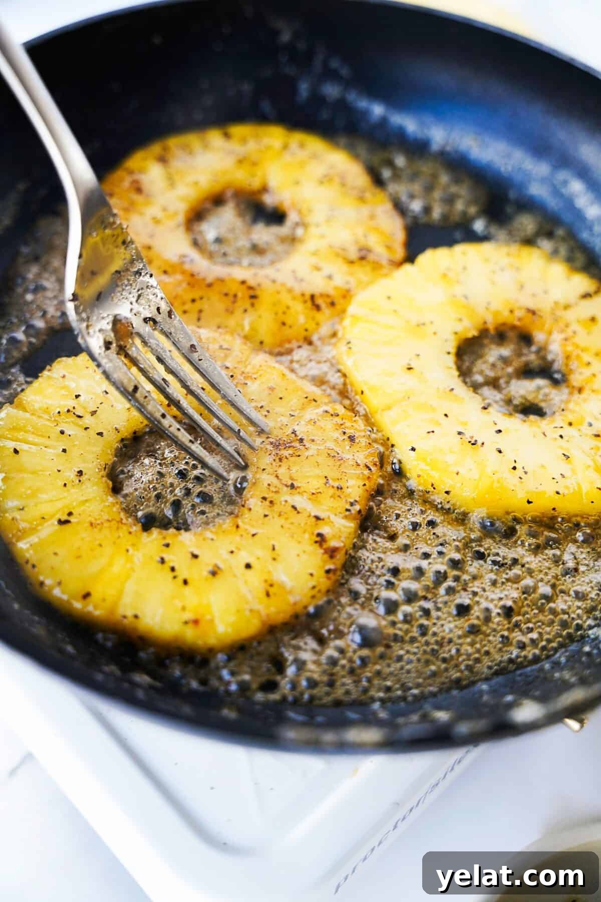 Spicy Pineapple Tart Recipe: Sweet and Tangy Baked Cookies 8 cast iron skillet cooking spicy pineapple slices in butter with fork preparing to flip over to caramelize on the other side