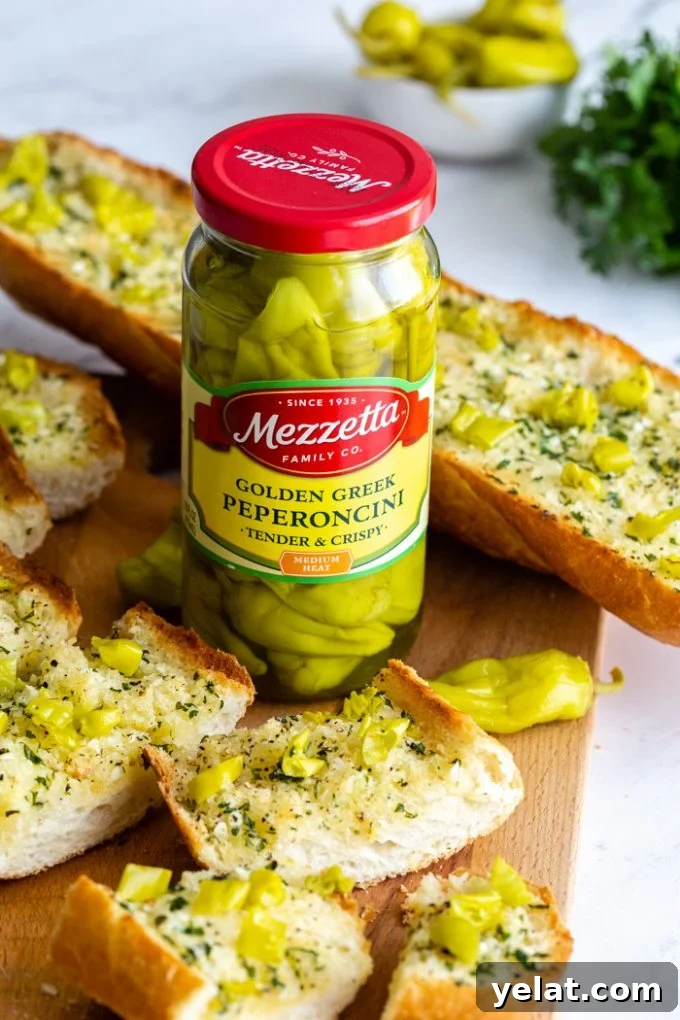 sliced garlic bread topped with chopped peperoncini peppers. focus of the photos is on a jar of mezzetta golden greek peperoncini