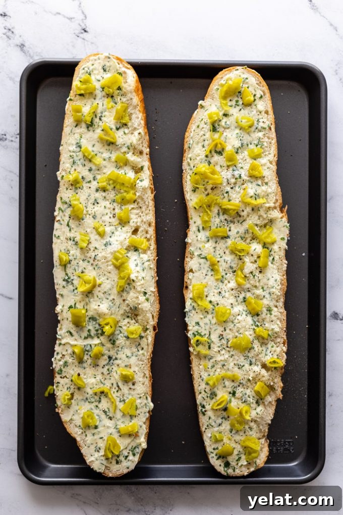 2 loaf halves of garlic bread topped with chopped peperoncini peppers. on a baking tray