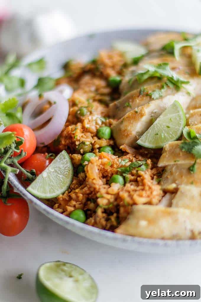 Authentic Mexican Cauliflower Rice Recipe for Flavorful Low-Carb Meals 6 A bowl filled with whole30 mexican rice and chicken, garnished with limes and cilantro.