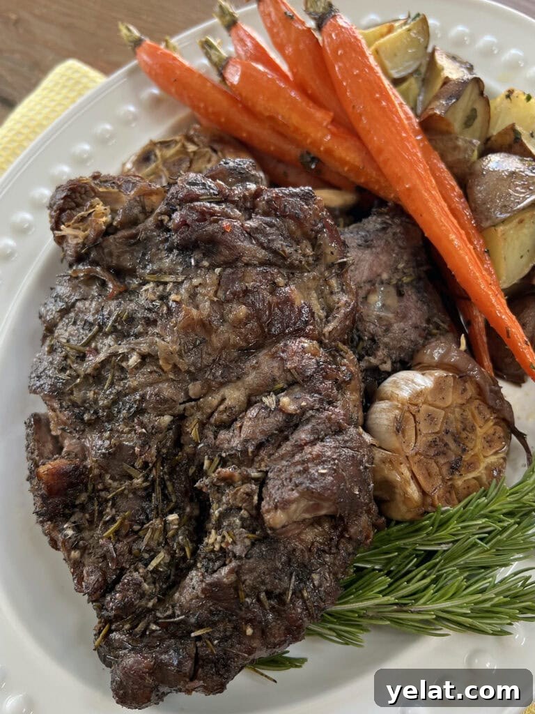 Slow-Roasted Mediterranean Lamb Shoulder Recipe 14 Slow Roasted Lamb Shoulder on white platter with rosemary sprigs, roasted carrots, roasted garlic and roasted potatoes.