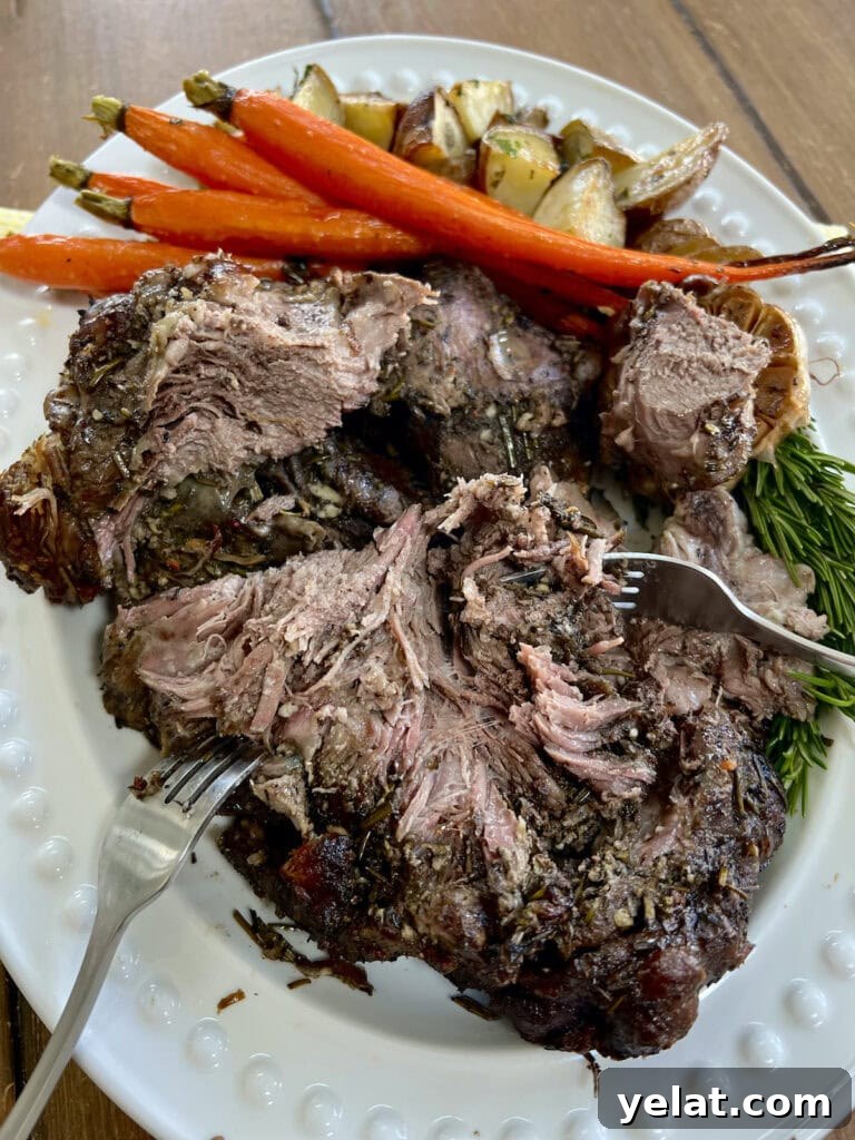 Slow-Roasted Mediterranean Lamb Shoulder Recipe 15 Slow Cooked Boneless Mediterranean Lamb Shoulder on white platter with rosemary sprigs, roasted carrots, roasted garlic and roasted potatoes–pulled with two forks.