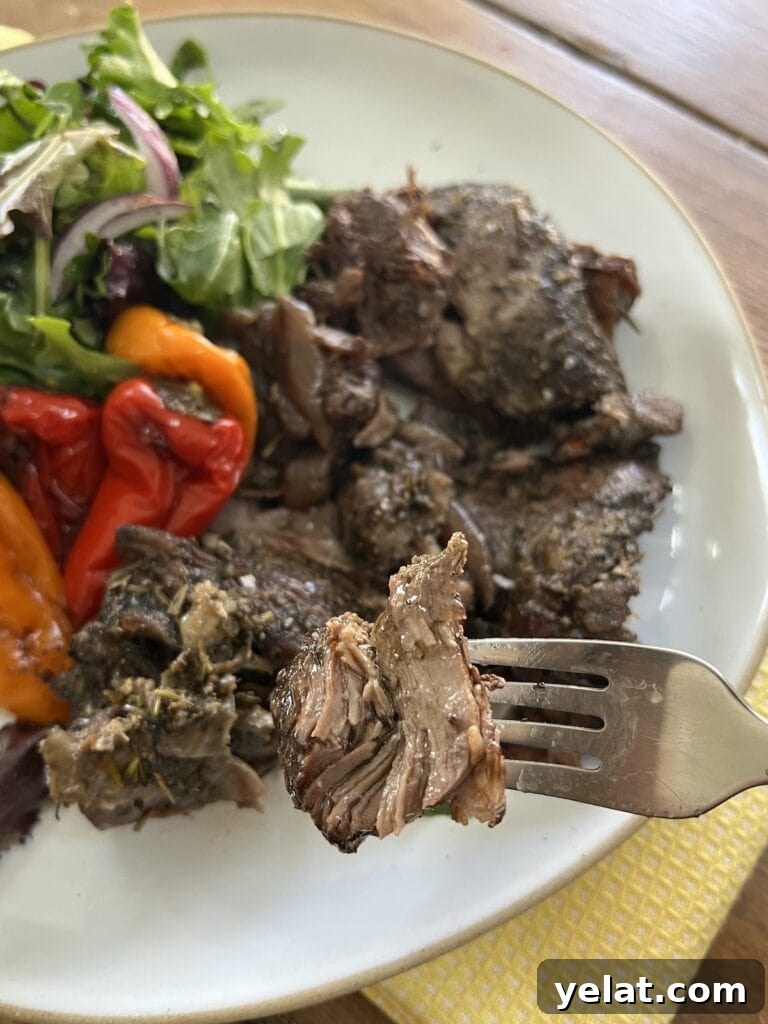 Slow-Roasted Mediterranean Lamb Shoulder Recipe 16 Close up of slow roasted lamb shoulder on fork with lamb and roasted vegetables in the background.