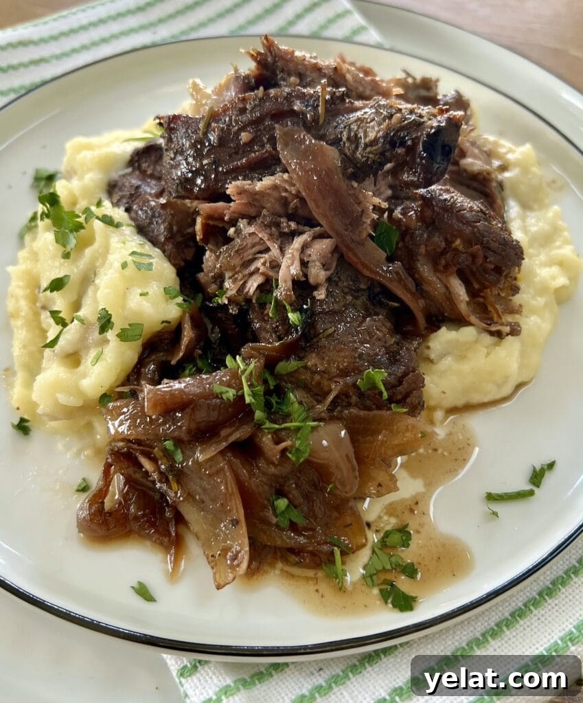 Slow-Roasted Mediterranean Lamb Shoulder Recipe 17 Slow Cooked Boneless Mediterranean Lamb Shoulder with sauce and onions over mashed potatoes on white plate.