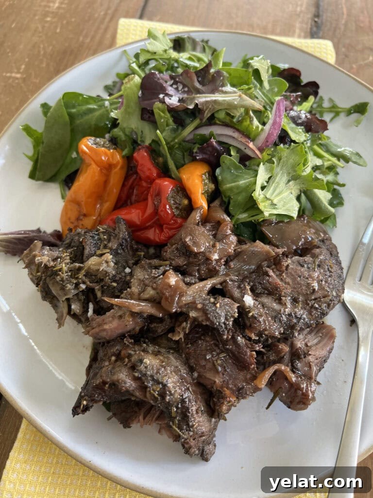 Slow-Roasted Mediterranean Lamb Shoulder Recipe 3 Slow Cooked Boneless Mediterranean Lamb Shoulder on white platte with roasted peppers and mixed green salad with fork.