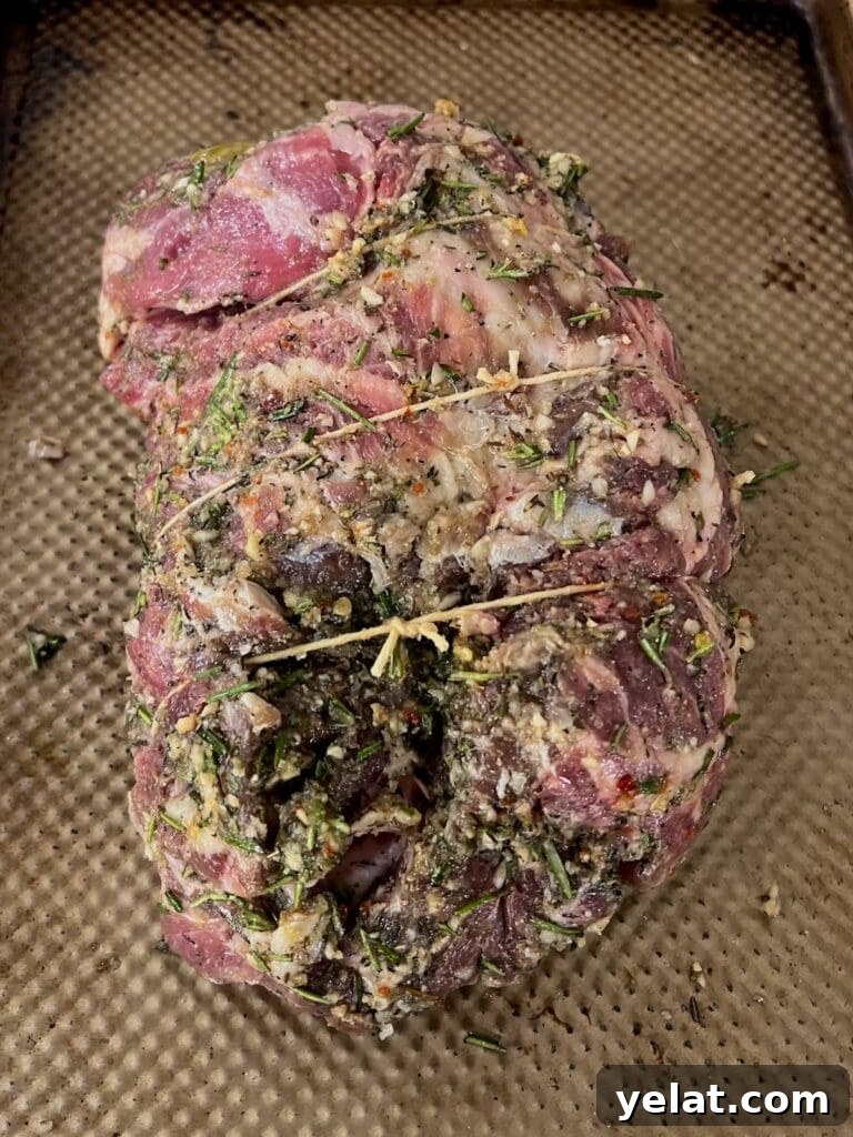 Slow-Roasted Mediterranean Lamb Shoulder Recipe 9 Garlic herb marinated meat tied up with butcher's twine on sheet pan.