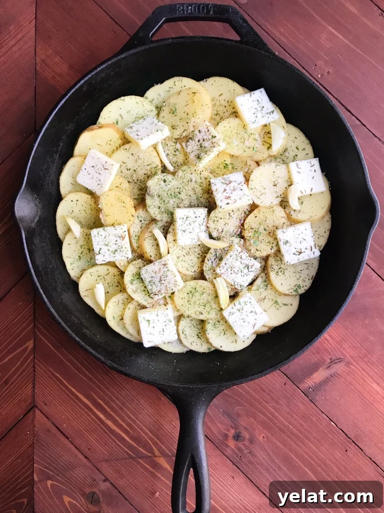 Sliced potatoes with butter pats and garlic in a cast iron skillet
