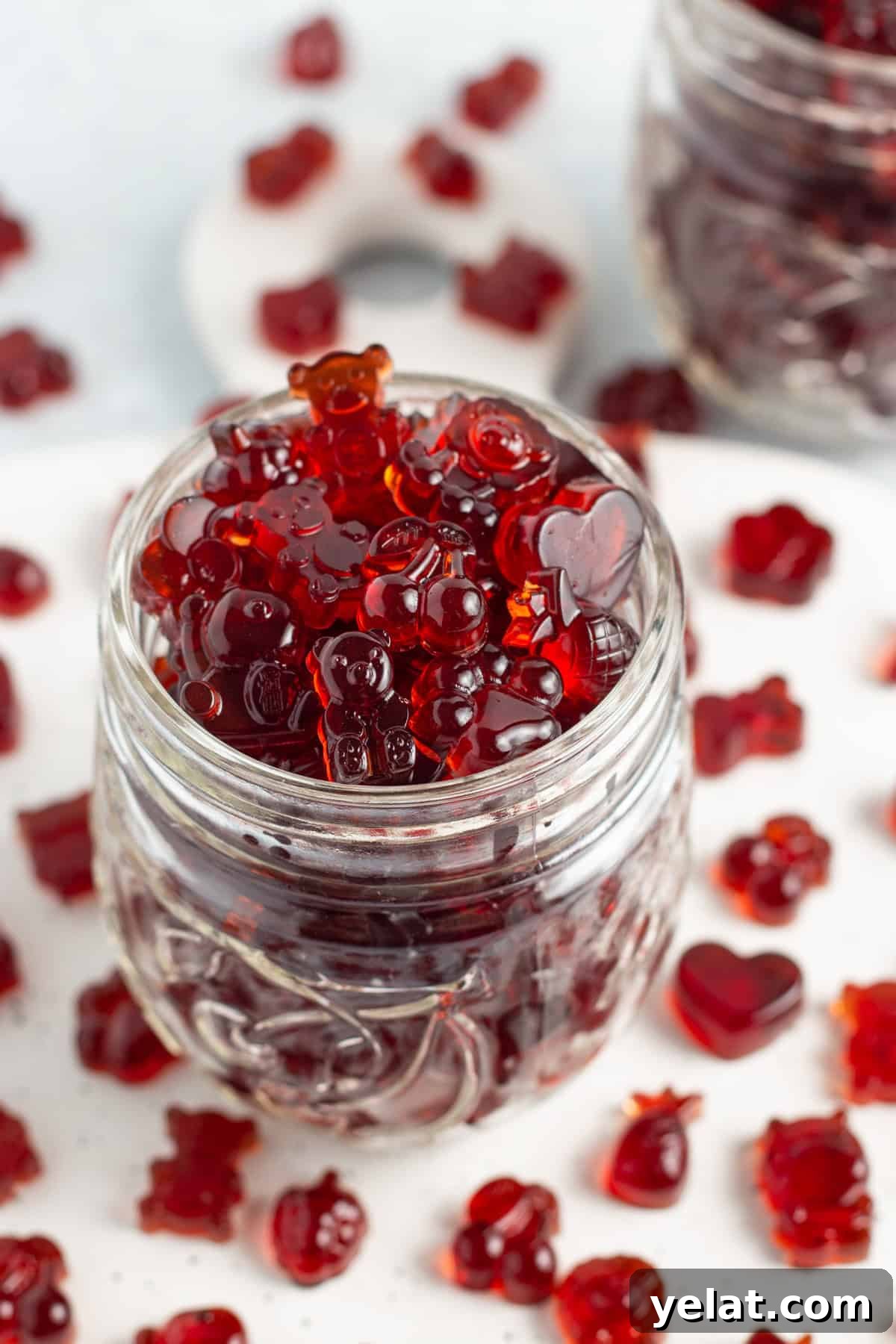 Tart Cherry Gummies for Sleep, Recovery & Joint Support 3 Close-up, overhead, angled view of a glass jar overflowing with bright red tart cherry gummies on a white countertop.
