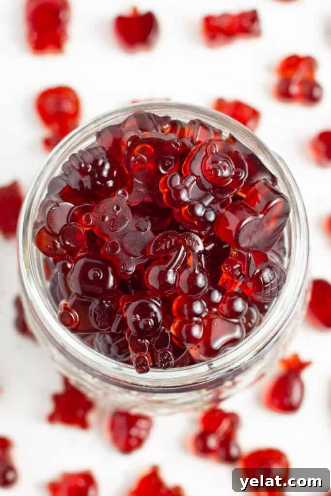 Tart Cherry Gummies for Sleep, Recovery & Joint Support 5 Close-up, overhead view of a glass jar overflowing with bright red gummies on a white countertop.