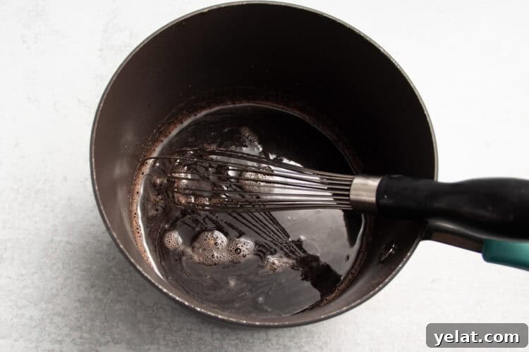 Tart Cherry Gummies for Sleep, Recovery & Joint Support 8 Overhead view of a black saucepan with tart cherry juice, lemon juice, lime juice, honey, and a whisk on a white countertop.