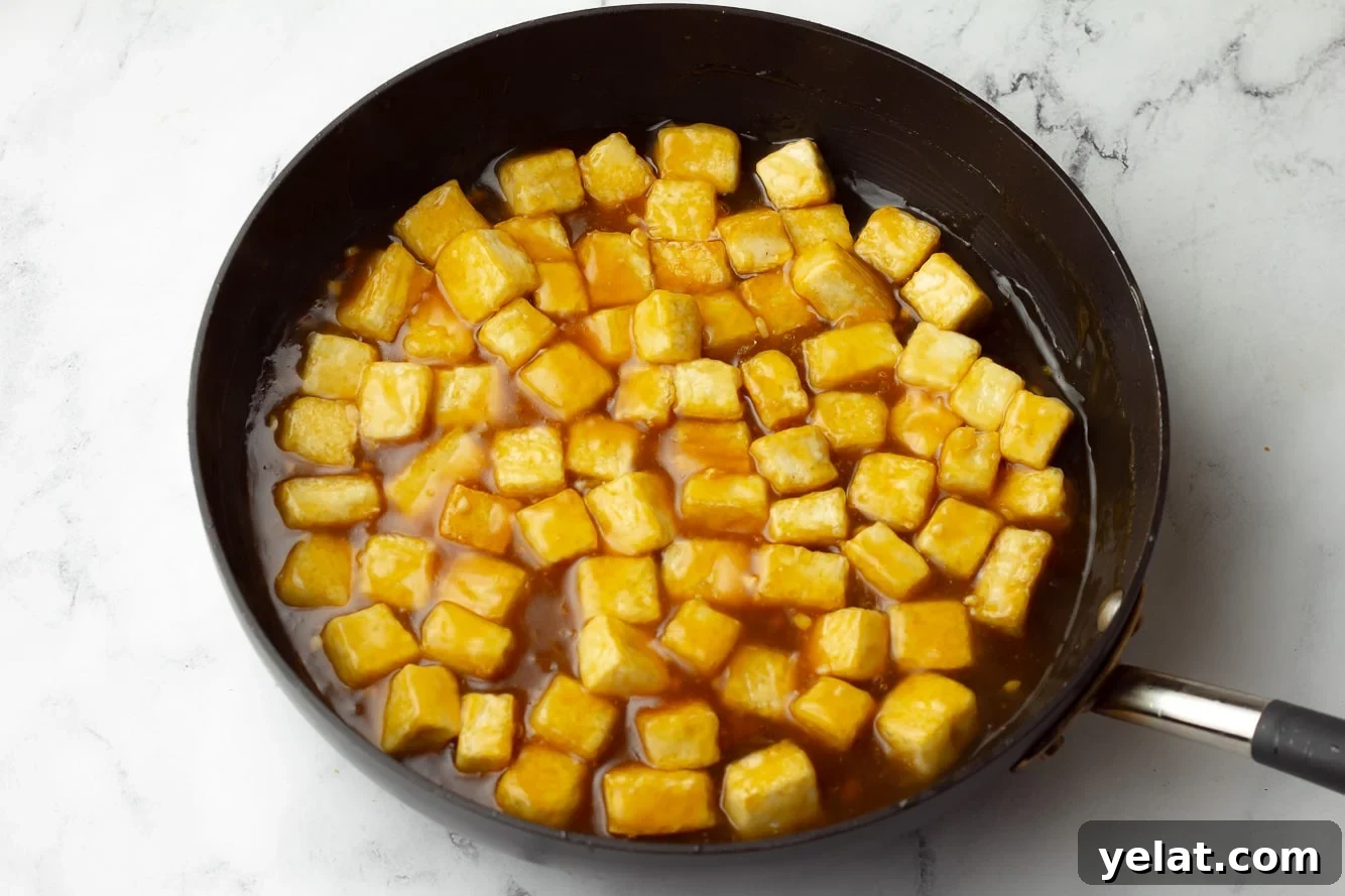 baked tofu cubes in a black skillet with orange sauce.