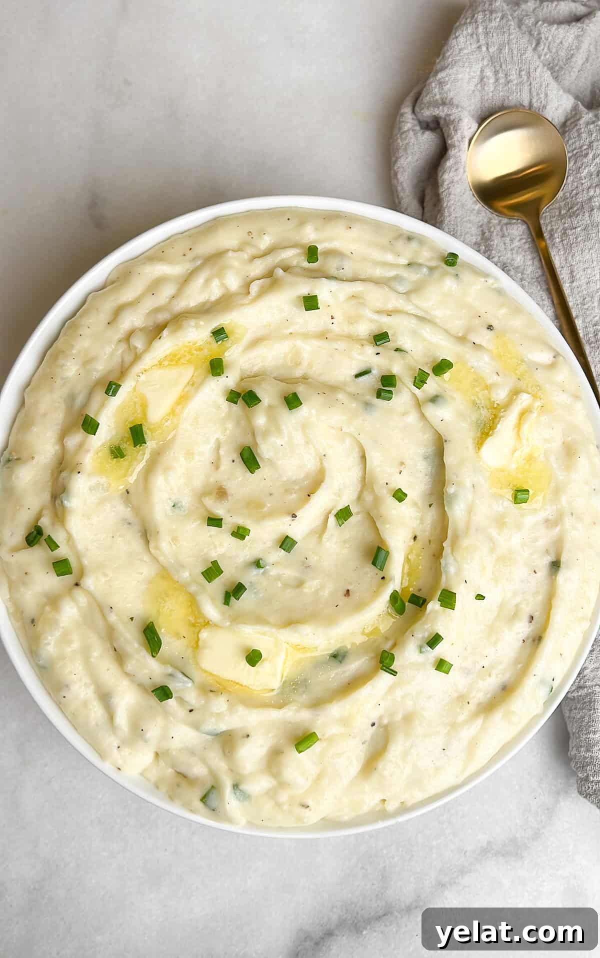 Overhead view of a bowl of Boursin mashed potatoes next to a gold spoon