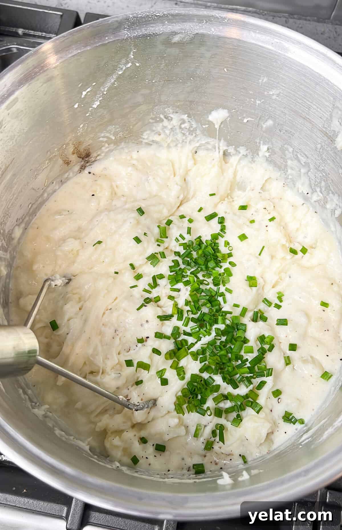 Adding chives to the mashed potatoes in a pot