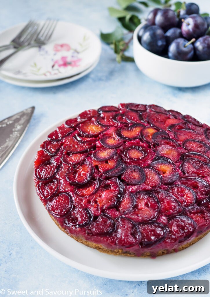Sticky Plum Upside-Down Cake Recipe for Fall Baking 2 Plum Upside Down Cake on white dish with fresh plums in background.