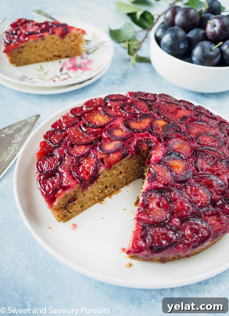 Sticky Plum Upside-Down Cake Recipe for Fall Baking 4 Plum Upside-Down Cake on white dish with slice removed to the side.