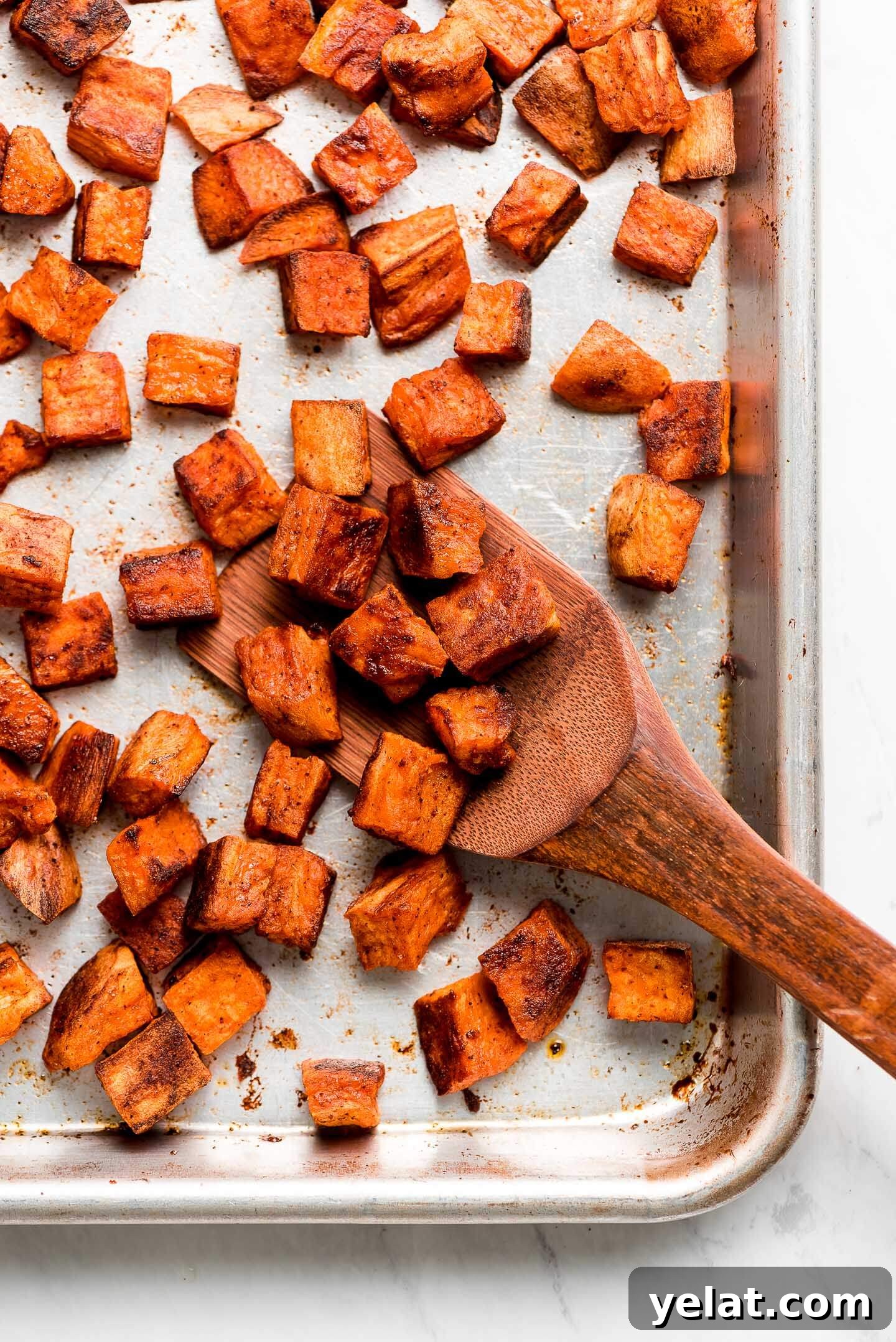 Crispy Roasted Sweet Potatoes with Garlic and Herbs 2 Cubed Roasted Sweet Potatoes on a baking sheet with a wooden spatula scooping some up.